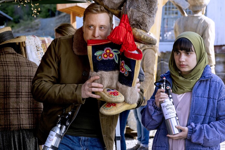 Harry Vanderspeigle (Alan Tudyk) holds embroidered boots next to Sahar (Gracelyn Awad Rinke) who holds 'manticide spray' on Resident Alien Episode 408.