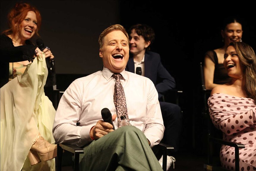 Resident Alien Cast Alan Tudyk Alice Wetterlund Sara Tomko laughing on stage