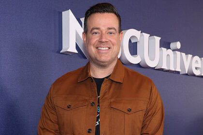 Carson Daly smiling as he stands on an NBC red carpet