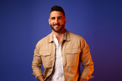 Paul Swan smiling while standing in front of a dark blue backdrop