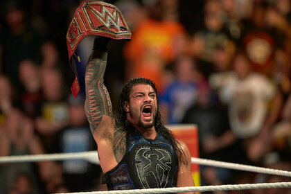 Roman Reigns lifts his belt above his head in a moment of passion