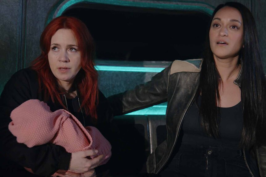 D'Arcy Bloom holds a baby next to Asta Twelvetrees on Resident Alien Episode 308.