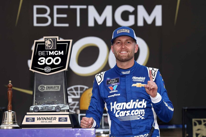 William Byron smiles and poses next to his NASCAR Xfinity Series BetMGM 300 trophy.