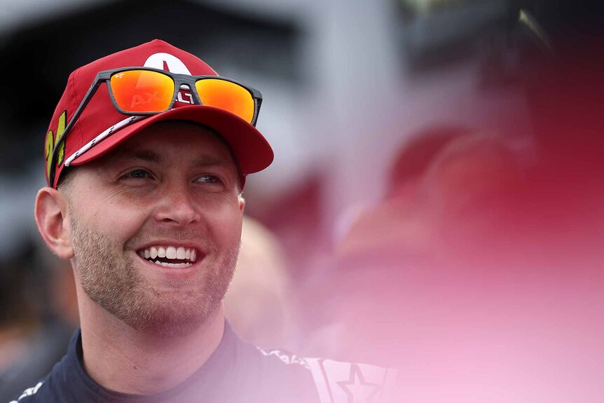 William Byron smiles in a red hat and glasses.