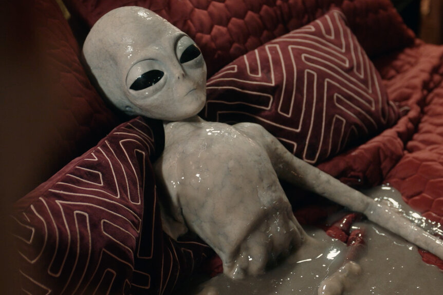 A grey alien lays in a pool of goop on Resident Alien Episode 402.