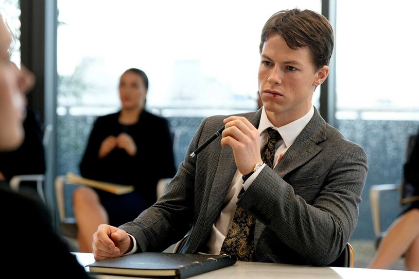 The Rainmaker star Milo Callaghan as Rudy Baylor in a suit with a split lip